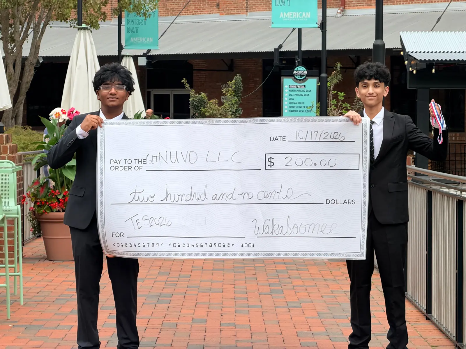 Two Nuvo founders in suits holding a large prize check made out to Nuvo LLC at TES 2026